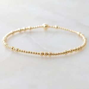 Minimalist golden beaded bracelet with varied size beads on white marble background