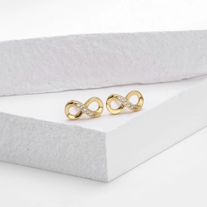 Detail of gold infinity stud earrings featuring white zircon pavé on a stone pedestal