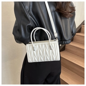 Detailed view of a white quilted crossbody bag with adjustable strap worn by a model
