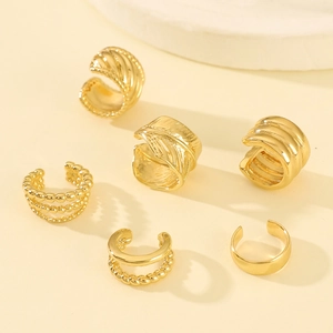 Set of six gold ear cuffs with textured leaf and braided designs on a warm background