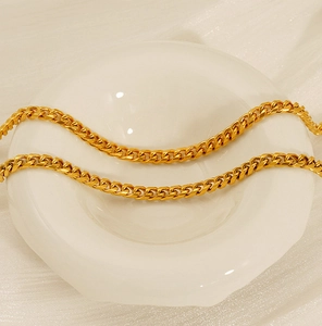 Polished 18K gold stainless steel Cuban link chain laid on a white ceramic display tray