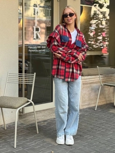 Gros plan sur une chemise à carreaux rouge et noir portée avec un jean dans un café en plein air