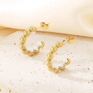 Detailed view of U-shaped gold earrings with shell pearls and textured metallic finish