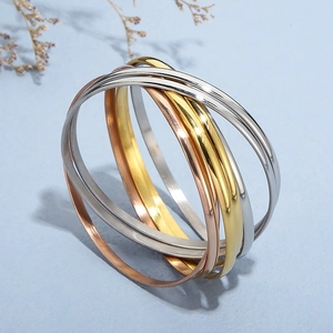 Polished interlocking gold silver and rose gold steel bracelets on sandy background
