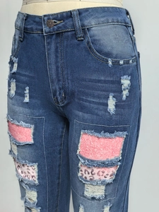 Dettaglio dei jeans blu strappati con paillettes rosa e inserti in stampa leopardata