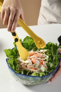 Detail of yellow cat paw silicone food tongs picking up salad with shrimp and lettuce