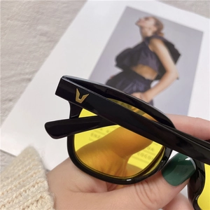 Detail of black frame sunglasses with yellow lenses and a gold V-shaped logo on the temple