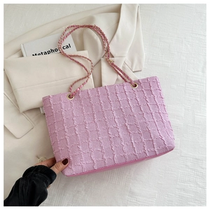 Detailed view of pink quilted tote bag with golden woven chain strap held against blazer