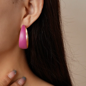 Detail of pink enamel C-shaped hoop earrings with gold lining shown on model