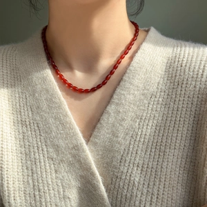 Detailed close-up of a red agate beaded necklace on a model wearing a white knit cardigan