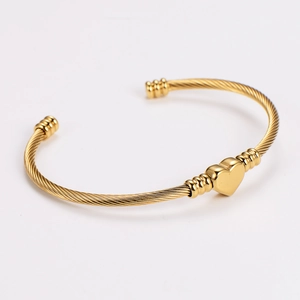 Detail of golden woven twisted rope bracelet with a polished heart charm on white backdrop