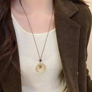 Detail of tiger eye stone pendant necklace layered with golden rings on a brown cord