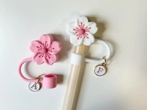 Detail of pink and white cherry blossom silicone straw covers with gold letter charms
