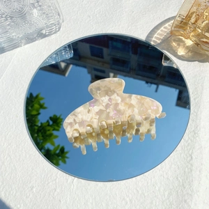 Iridescent cream hair claw clip detail reflecting a blue sky on a circular mirror surface