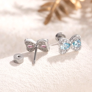 Elegant silver bow stud earrings with pink and blue gemstones on beige velvet