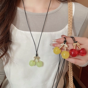 Detailed view of red, yellow, and green cherry pendants with golden leaves on wax cords