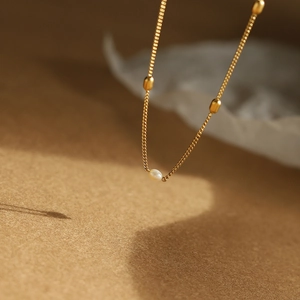 Macro detail of minimalist freshwater pearl necklace with 18K gold plated beads and fine chain