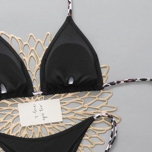 Detail of black bikini set with pink leopard print ties on decorative gold mat
