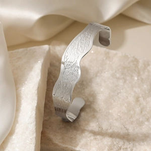 Silver wavy open bangle in brushed stainless steel on a white stone base with silk