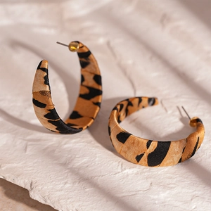 Detailed close-up of leopard print fabric C-shaped earrings on a textured stone surface
