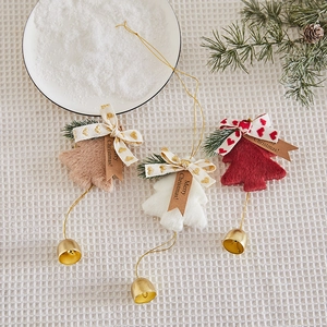 Three plush Christmas tree ornaments with ribbons and golden bells on a snowy background