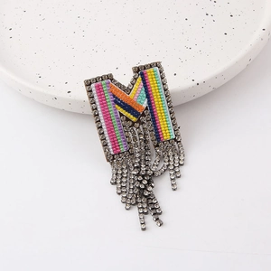 Macro detail of M-shaped brooch with colorful beads, silver rhinestones and tassels