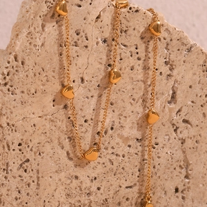 Detail view of 18K gold plated heart charms on a delicate chain over natural stone