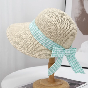 Detail of summer straw hat featuring houndstooth ribbon bow on a wooden stand