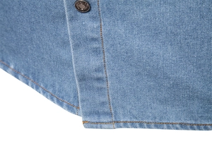 Detailed macro view of the blue denim shirt hem showing stitching and a fashion button
