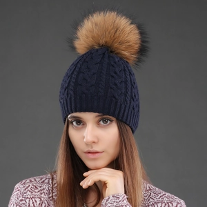 Close-up of navy blue cable knit wool hat with premium brown raccoon fur pom-pom detail