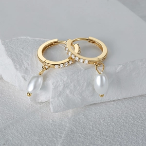 Detailed macro view of gold-plated pearl drop earrings with sparkling zircon inlay