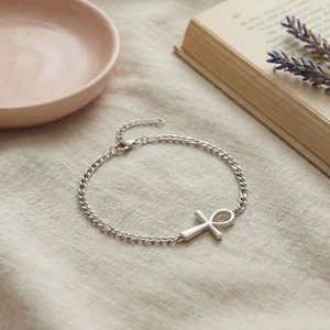 Silver Ankh cross bracelet with Cuban chain on linen fabric and aesthetic background