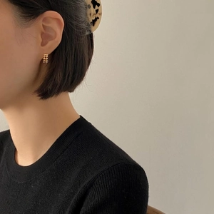 Nahaufnahme einer kleinen minimalistischen Gold-Creole an einem Model in schwarzem Strick