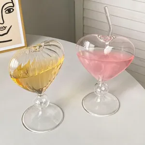 Elegant heart shaped wine glasses with straws and vertical ribbing on white table