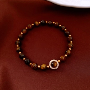Gros plan du bracelet en pierres œil de tigre avec pendentif doré sur fond de soie