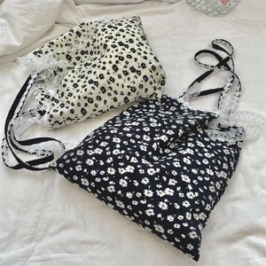 Close-up of floral canvas tote bags with white lace straps on a soft fabric surface