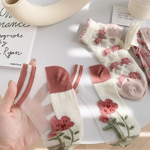 Detail einer transparenten Netzsocke mit Blumenstickerei, die per Hand präsentiert wird