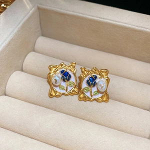 Detail of French vintage gold plated floral stud earrings with blue enamel rose and pearl