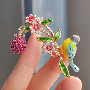 Macro detail of enamel bird brooch with raspberries and cherry blossoms on gold base