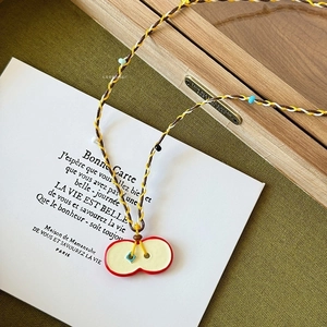 Détail d'un pendentif en forme de pomme rouge avec cordon de collier tressé coloré
