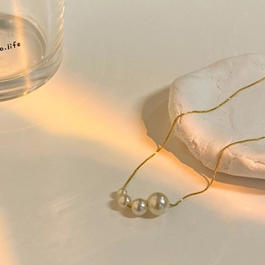 Détail d'un collier de perles plaqué or sur une pierre blanche sous une lumière chaude