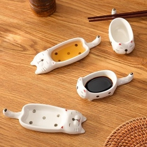 Detailed top view of four cat-shaped ceramic sauce dishes on a wooden dining table