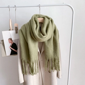Detailed texture of thick grass green mohair scarf with fringes hanging on a hanger