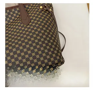 Detail of the brown tote bag featuring golden clover monogram pattern and metal hardware