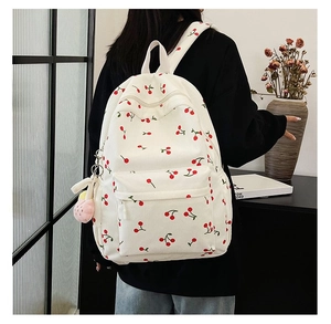 Rear view of corduroy cherry print backpack with plush pendant in a home setting