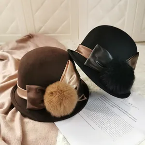 Detail of dark brown and black wool felt hats with large fur balls and satin bows