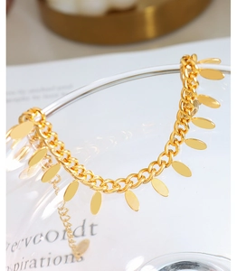 Detailed close-up of 18k gold plated titanium chain bracelet with leaf oval charms on glass