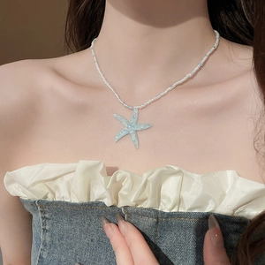 Close-up of a blue starfish pendant with matching white and blue beaded chain on a model