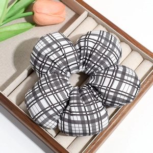Detailed view of a black and white plaid oversized floral hair tie in a wooden box