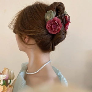 Detail view of a hair claw clip featuring dark red and sage green faux flower blossoms